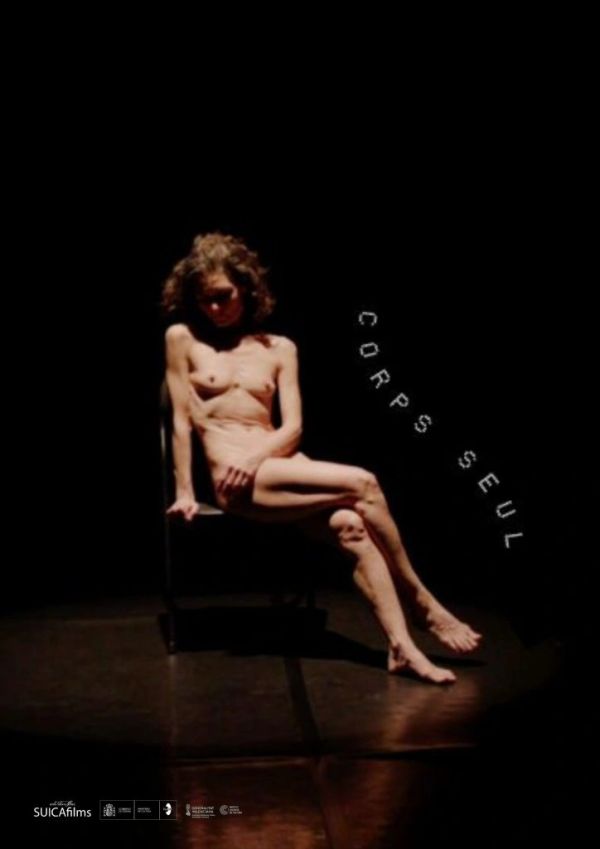Mujer desnuda sentada en una silla bajo luz tenue.
