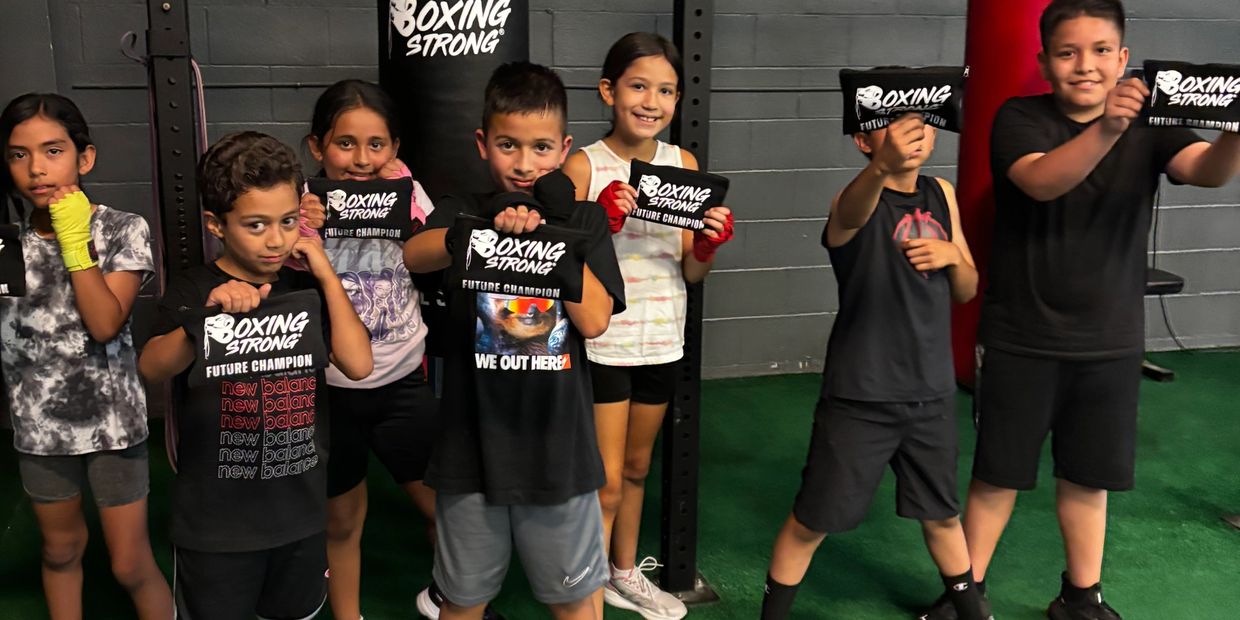 A group of kids showing "Boxing Strong" cards at a gym.
