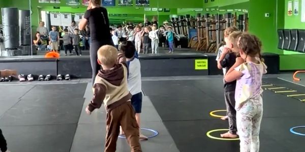 Children participating in a group activity in a gym with a female instructor.
