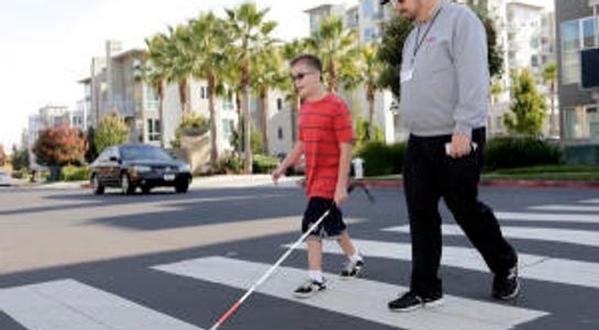 O&M teacher crossing the street with male student using a white cane.