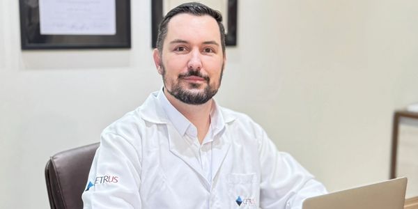 Homem de jaleco branco sentado em escritório.