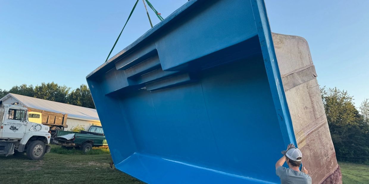 A man inspects a large blue fiberglass pool being lifted by a forklift outdoors.