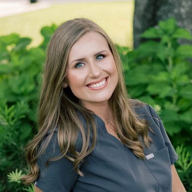 Smiling woman outdoors with greenery background.