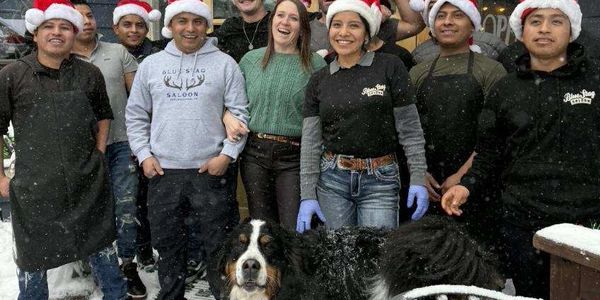 Group of people in Santa hats with a large dog in snowy outdoor setting.