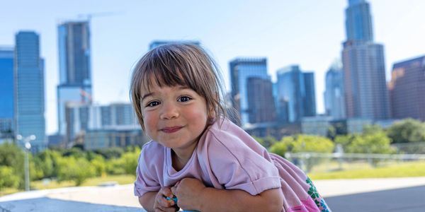 Smiling child leaning forward with city skyline background.
