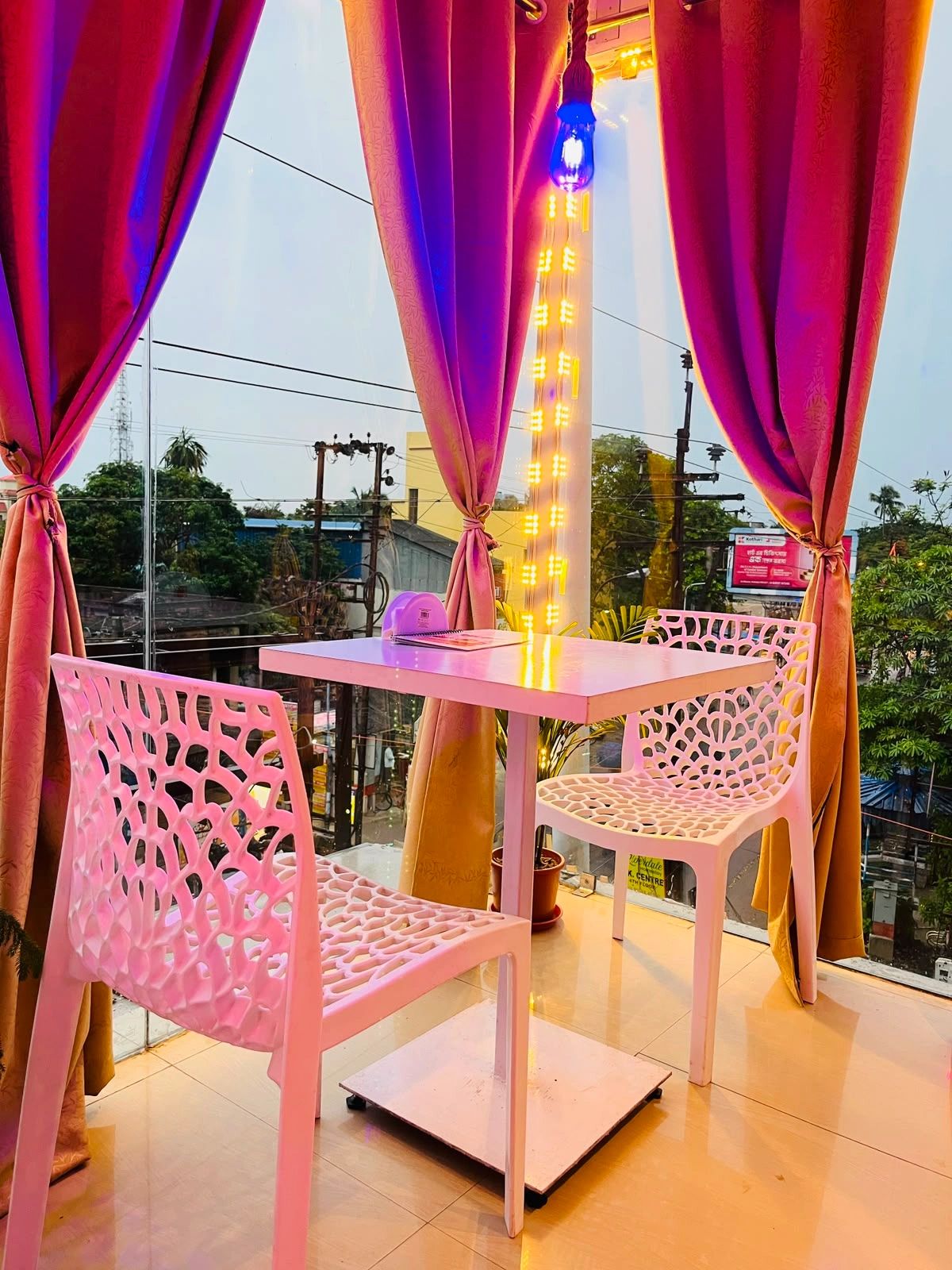 Cozy table setup with white chairs by large windows and curtains.