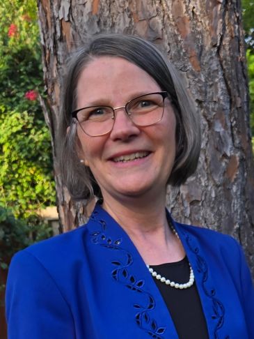 Woman in glasses and blue jacket smiling outside.