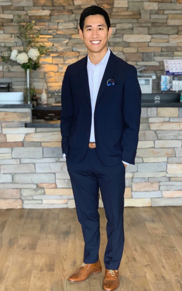 Smiling man in suit jacket standing against a stone wall.