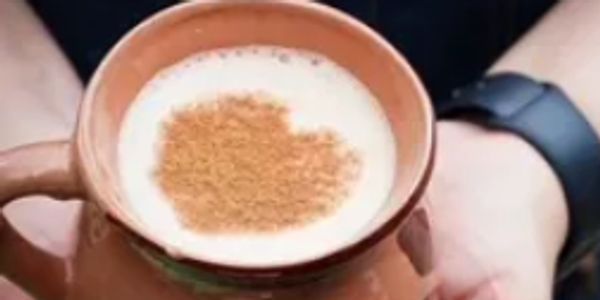 Hands holding a traditional cup with heart-shaped cinnamon on coffee foam.