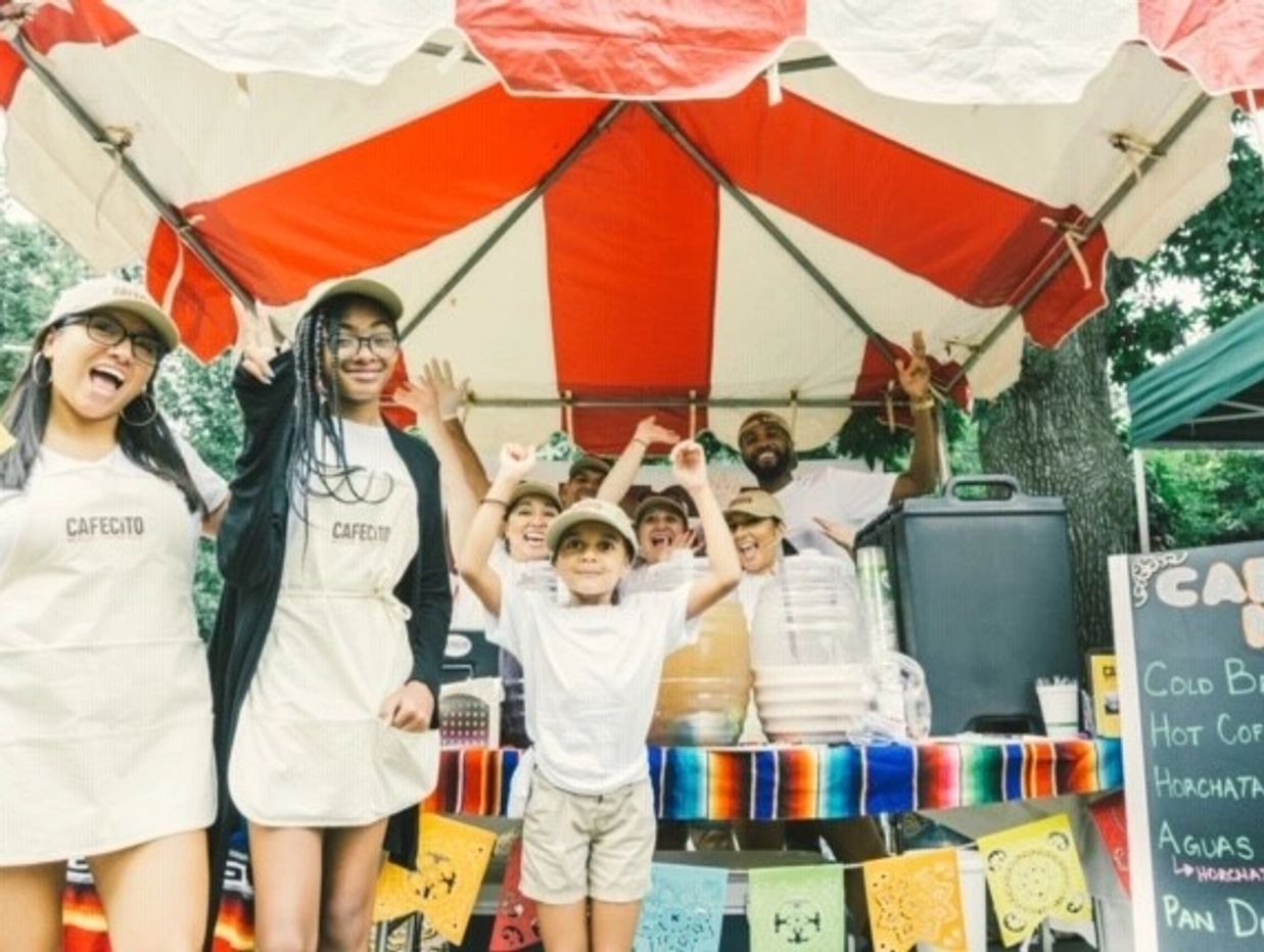 Group of cheerful people at a colorful coffee stand under a red and white canopy.