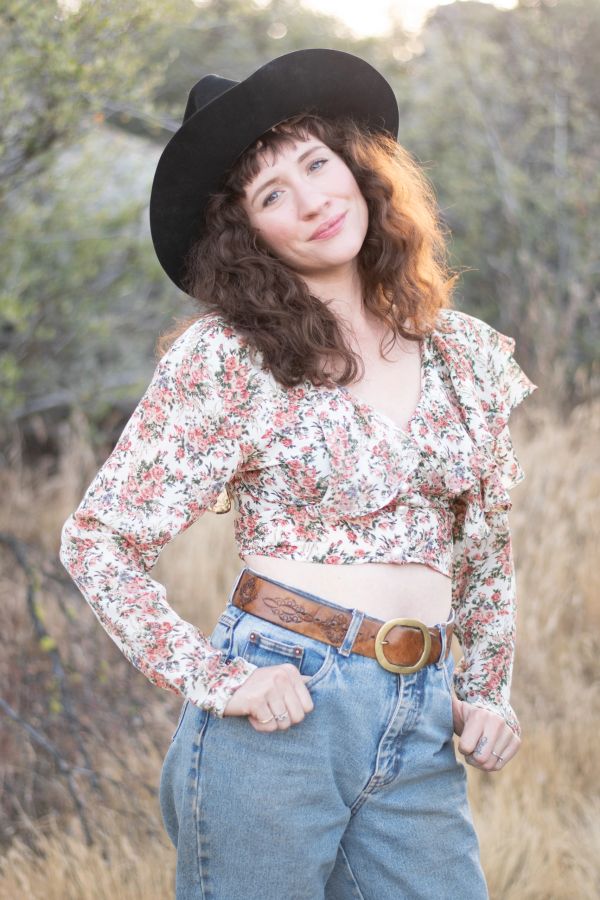 Woman in floral top and black hat smiling outdoors.