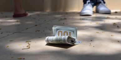 Rolled-up hundred-dollar bills on the ground in sunlight.