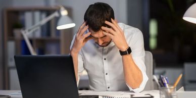 Stressed man holding his head while working late on a laptop.