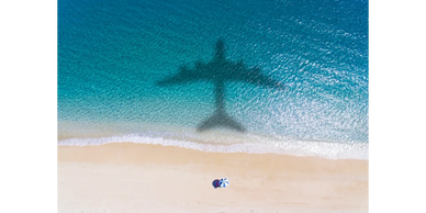 shadow of a plane flying over a golden sandy beach over a blue sea