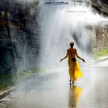 Person in yellow dress walking through misty waterfall on urban street.