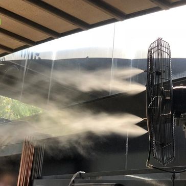 A fan blowing mist or vapor in an outdoor covered area.