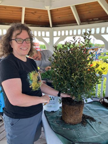 Woman holding a potted plant under a gazebo with gardening supplies.