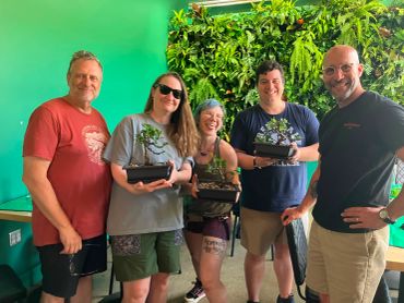 Group of five people holding bonsai trees indoors.