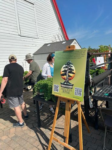 Signboard about Triplefoot Bonsai at an outdoor market on a sunny day.