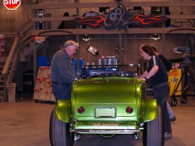 Two men inspecting a shiny green hot rod in a garage.
