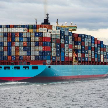 Large cargo ship loaded with colorful shipping containers at sea.