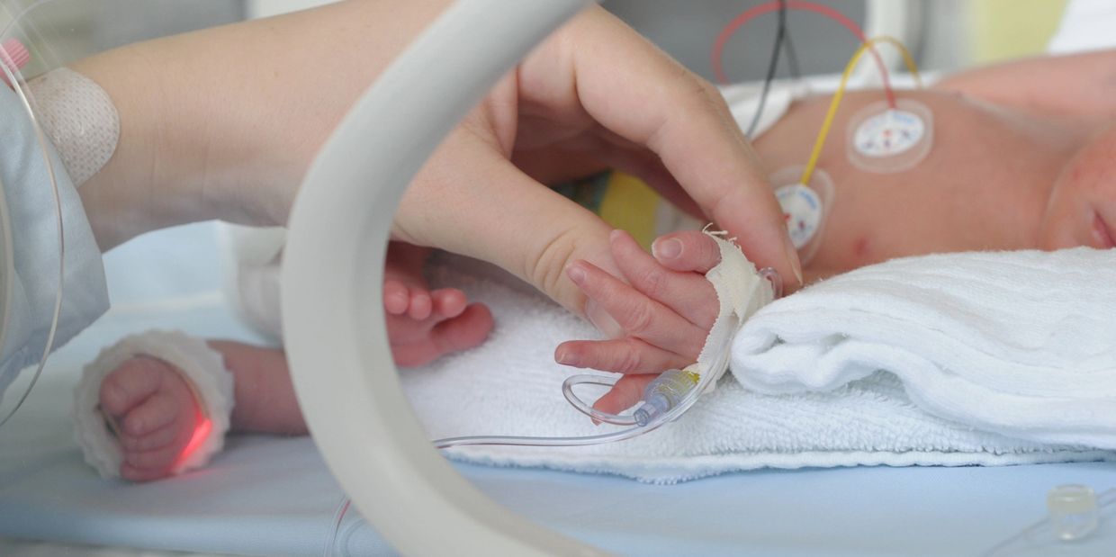Un bébé prématuré dans une incubatrice tenant le doigt d'un adulte.