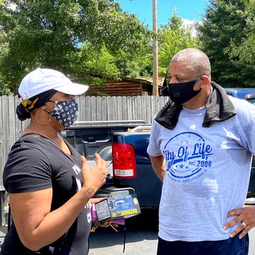 Two people wearing masks talk outdoors on a sunny day.