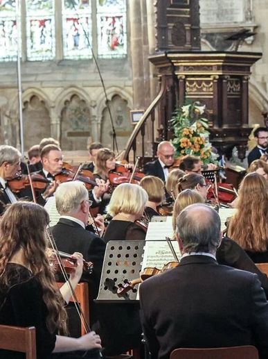 Orchestra performing inside a historic church with stained glass windows.