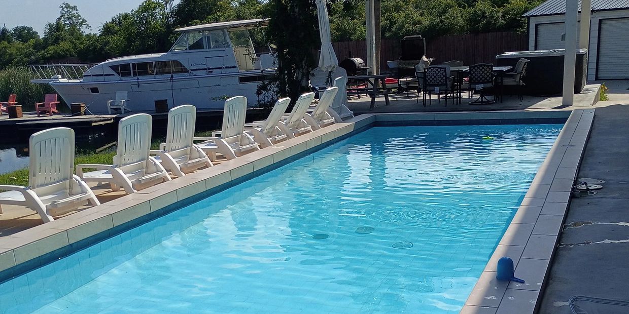 A clear blue swimming pool with white lounge chairs and a boat docked nearby.