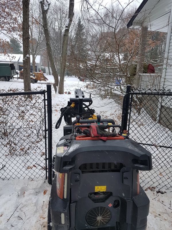 Rear view of mini skid steer clearing branches in tight yard.
