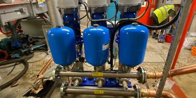 Blue potable water pressure vessels installed on a booster pump manifold.