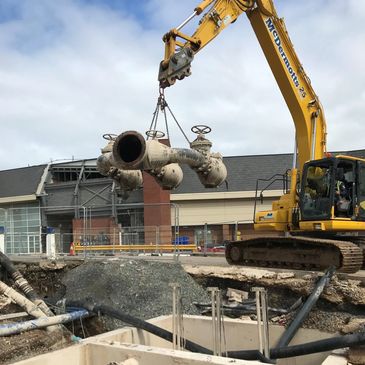 Excavator crane lifting a heavy non-return valve manifold for a Leicester project.