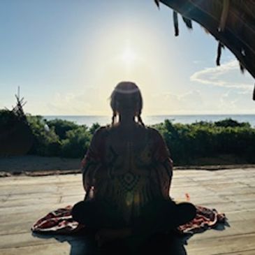 Person meditating facing the ocean during sunrise or sunset.