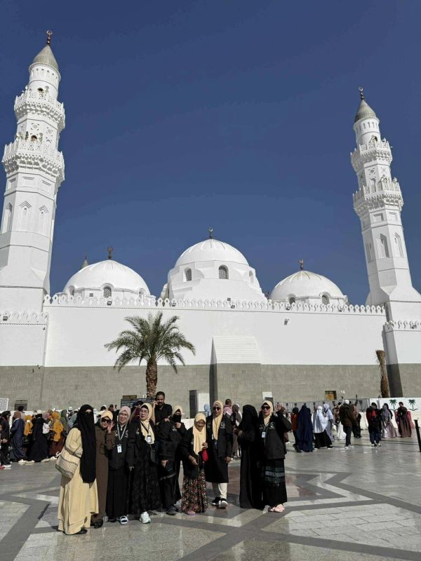 Group of people in front of a mosque with white domes and clear blue sky.