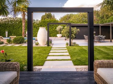 Modern garden with geometric stone pathway and seating areas framed by black wooden arches.