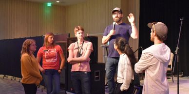 A group listening to a man speaking with a microphone indoors.