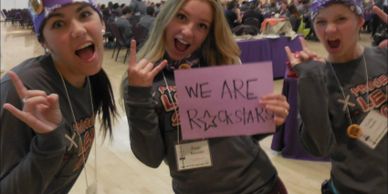 Three excited girls holding a sign that says 'We are rockstars'.