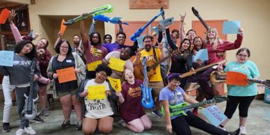 A lively group of people posing with colorful inflatable guitars and signs indoors.