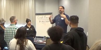 A man leads a workshop with a group of attentive participants in a conference room.