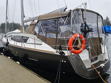 A sleek sailboat docked with a covered cockpit and orange lifebuoy.