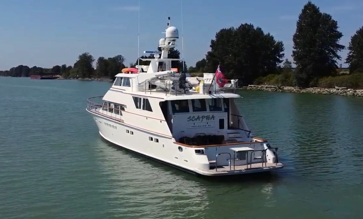 White yacht cruising on calm water near a tree-lined shore.