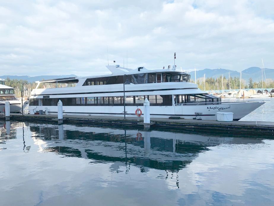 A large white yacht docked at a marina with mountains in the background.