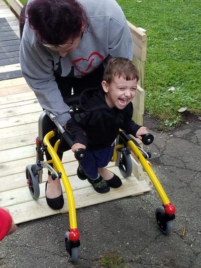 A child using a walker is joyfully supported by an adult outdoors.