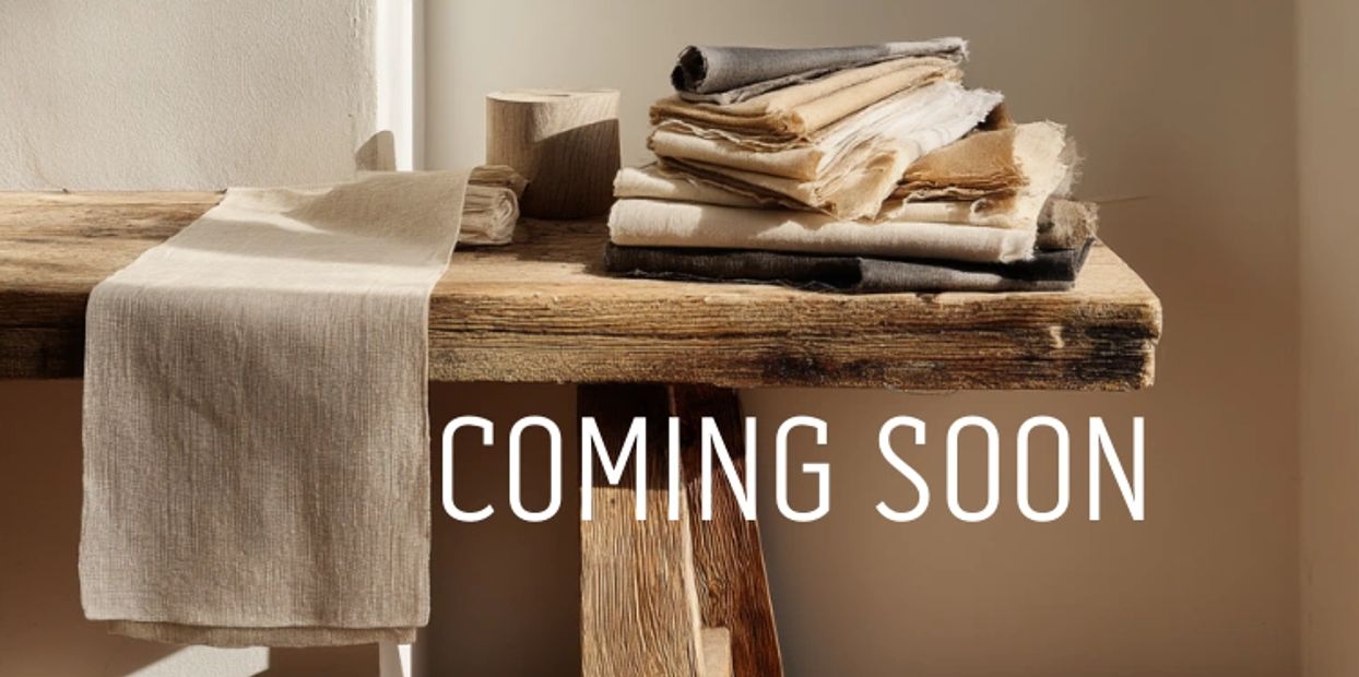 Stack of fabric with 'Coming Soon' text on a wooden table.