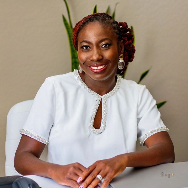 Smiling woman in white blouse sitting at a desk with a laptop and mouse.
