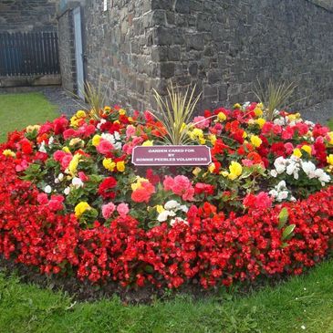 Colorful flower bed cared for by volunteers in front of a stone wall.
