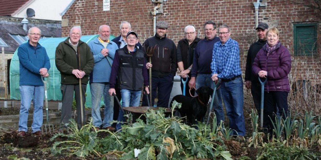 Group of people standing in a garden with gardening tools and a dog.