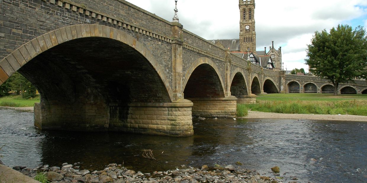 Stone arch bridge over a river with a clock tower in the background.