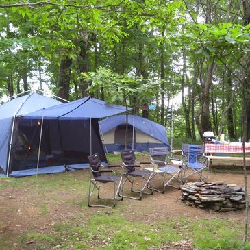 a camp in the forest with four chairs 