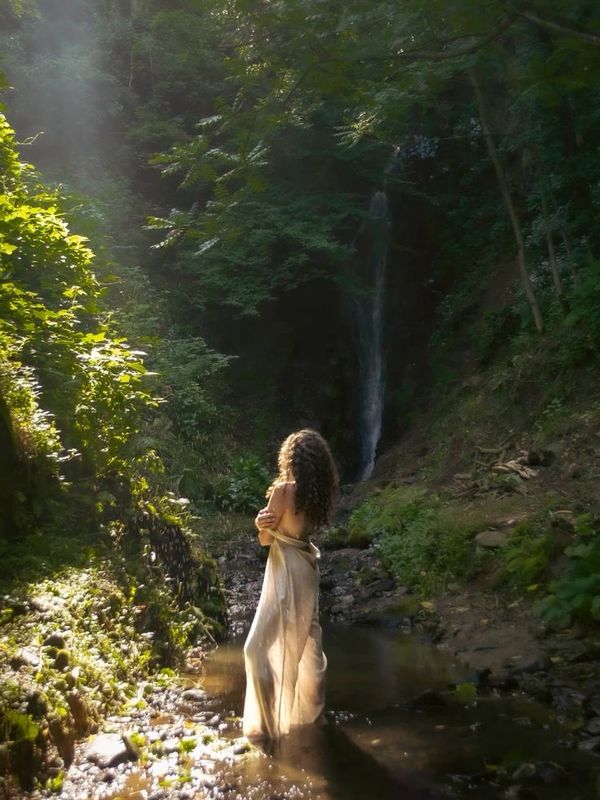 woman standing in the middle of a rainforest facing the sunlight and the waterfalls